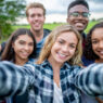 A group of multi-ethnic students taking a selfie outside.  They are dressed casually and having fun together in a group.